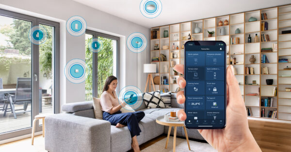 Frau sitzt im Wohnzimmer, davor ein Handy mit Bosch Smart Home App Ansicht
